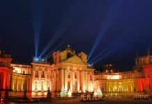 Christmas At Blenheim Palace Blenheim Palace façade glowing amber with search‑lights and Christmas trees