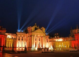 Christmas At Blenheim Palace Blenheim Palace façade glowing amber with search‑lights and Christmas trees