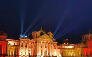 Christmas At Blenheim Palace Blenheim Palace façade glowing amber with search‑lights and Christmas trees