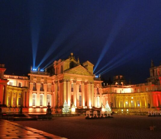 Christmas At Blenheim Palace Blenheim Palace façade glowing amber with search‑lights and Christmas trees