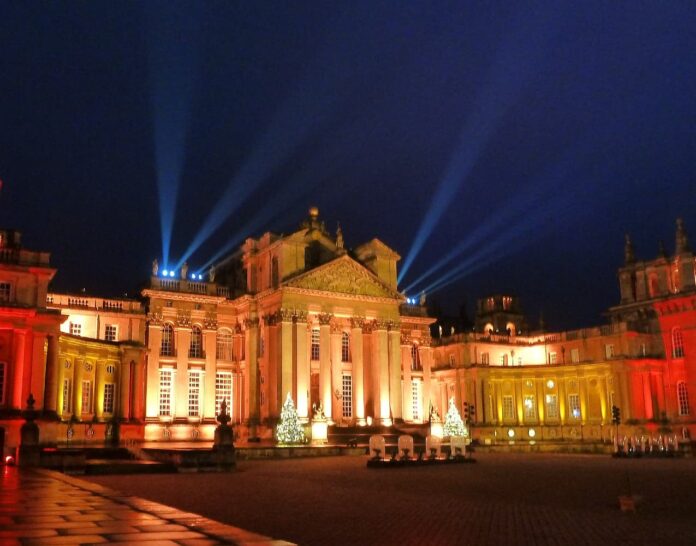 Blenheim Palace façade glowing amber with search‑lights and Christmas trees